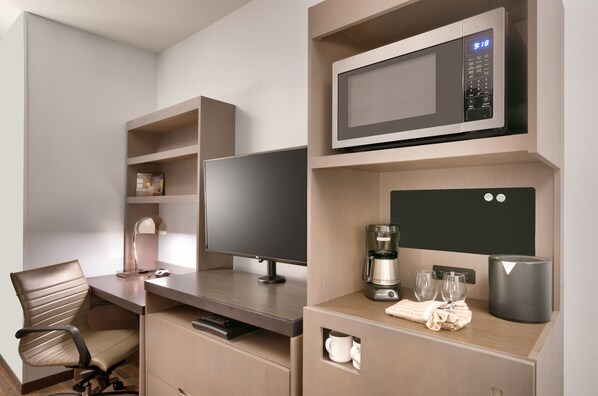 Una habitación de hotel moderna con televisión de pantalla plana, cafetera, microondas y un mueble pequeño.