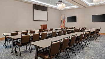 A conference room with long tables and chairs, flags, a podium, and a projector screen.