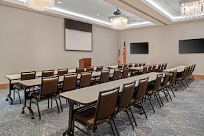 Une salle de conférence avec de longues tables et des chaises, des drapeaux, un pupitre et un écran de projection.