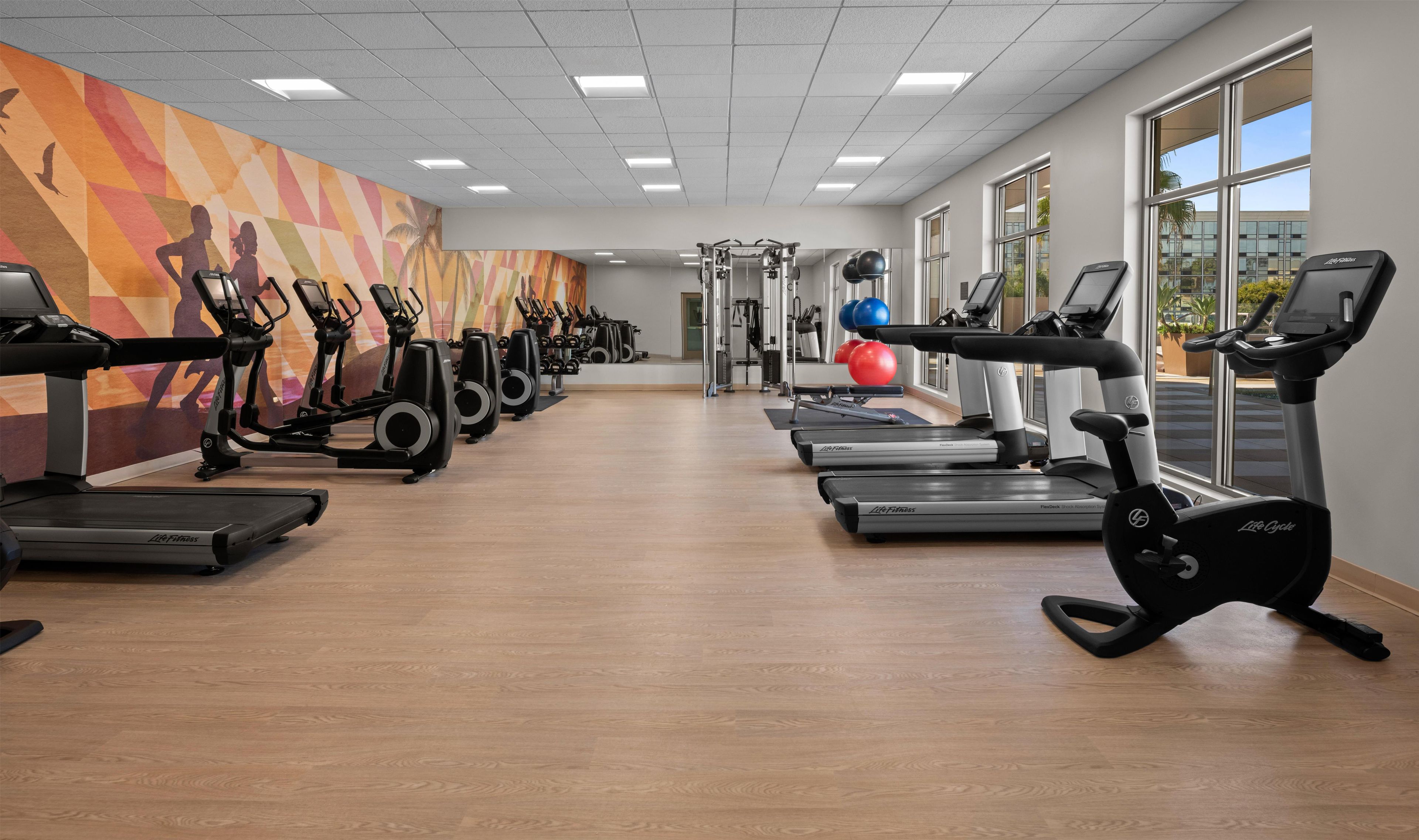 Ett gym med konditionsmaskiner, styrketräningsutrustning och en färgstark väggmålning.