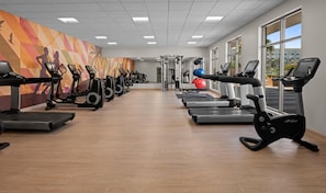 Un gimnasio con máquinas de cardio, equipo de pesas y un mural colorido.
