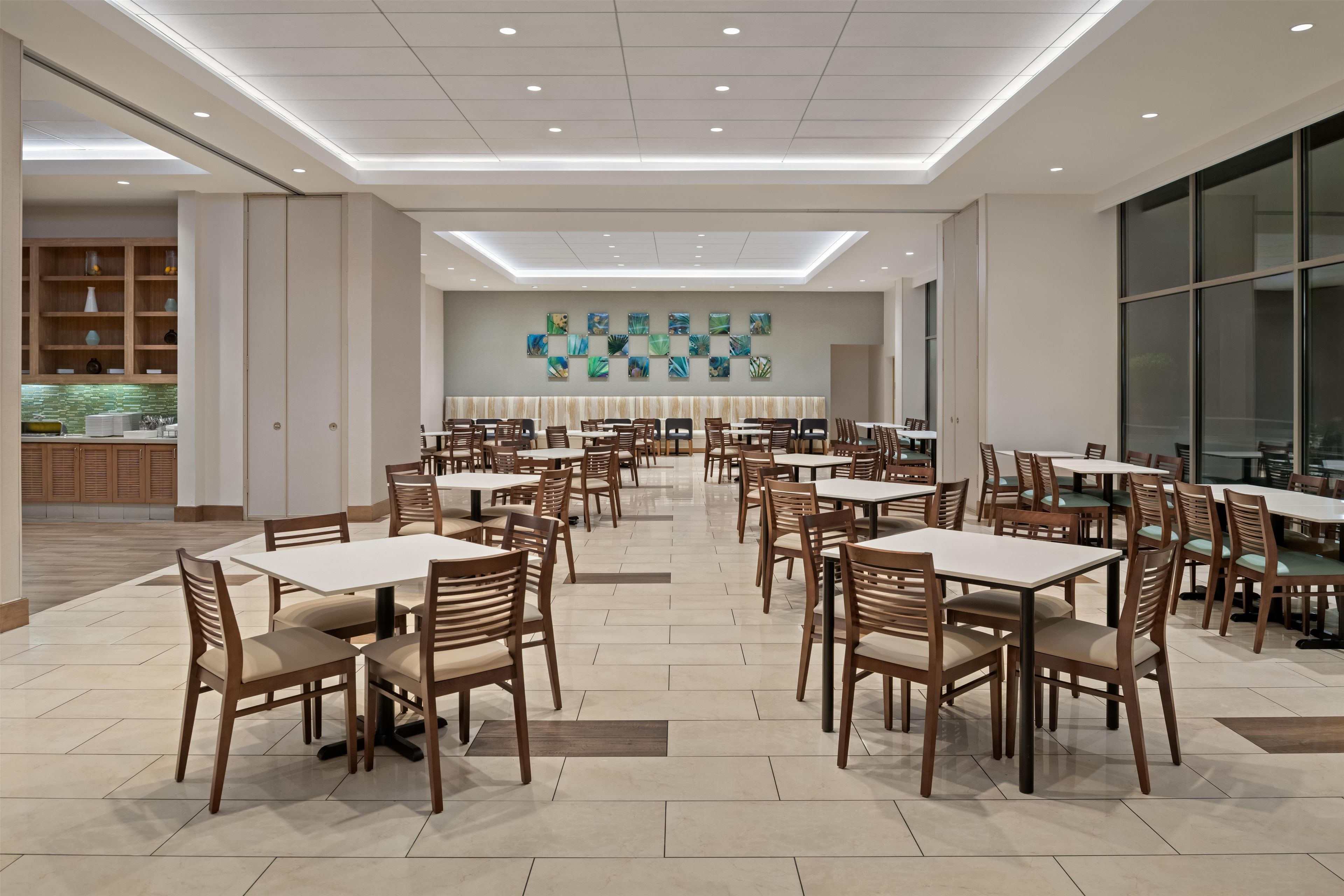 A spacious dining area with multiple tables and chairs, a modern ceiling design, and a wall with abstract art.
