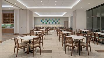 A spacious dining area with multiple tables and chairs, a modern ceiling design, and a wall with abstract art.