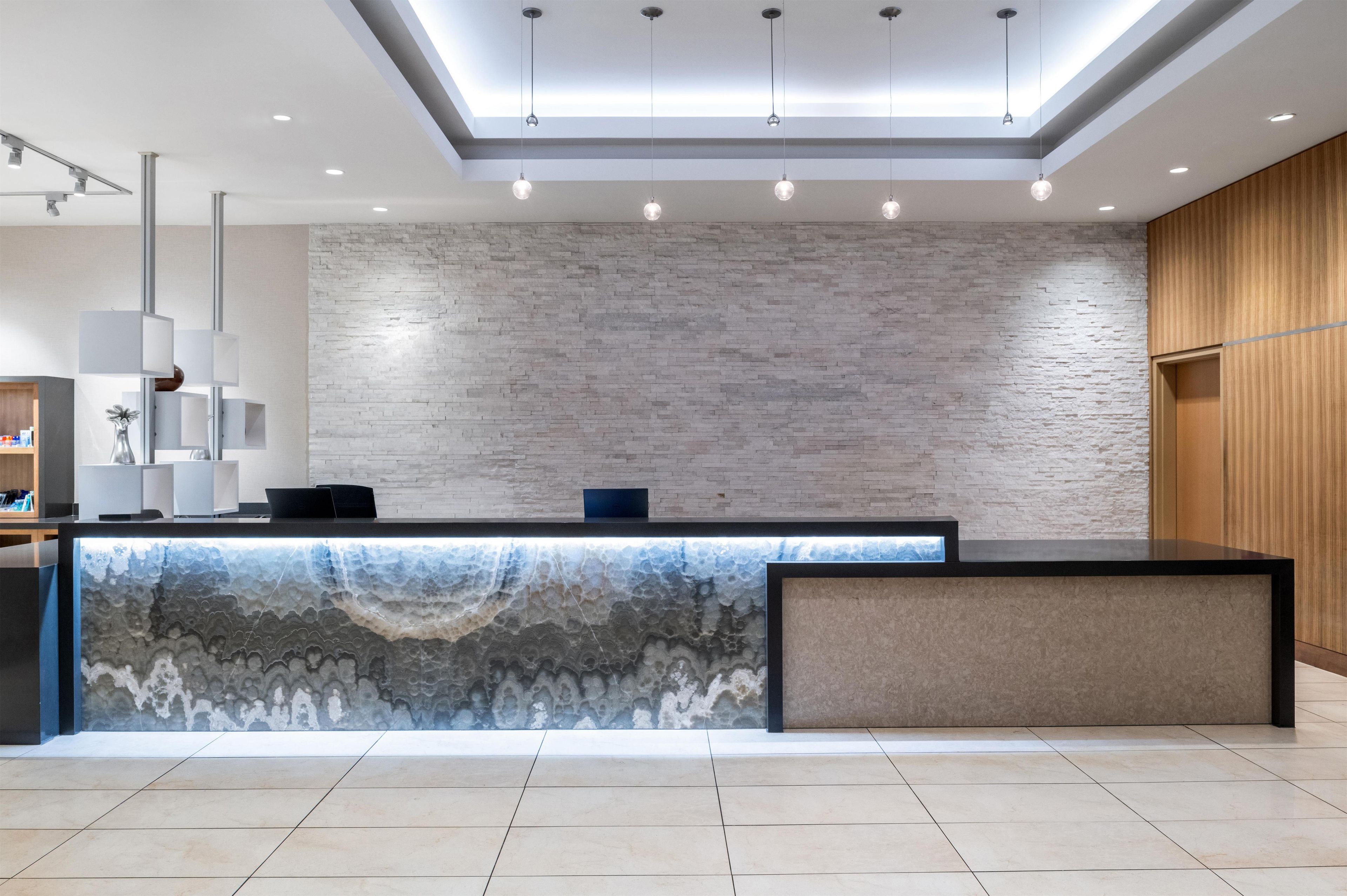 A reception desk with a stone-like textured wall behind it, a modern light fixture above, and a wooden panel on the right.