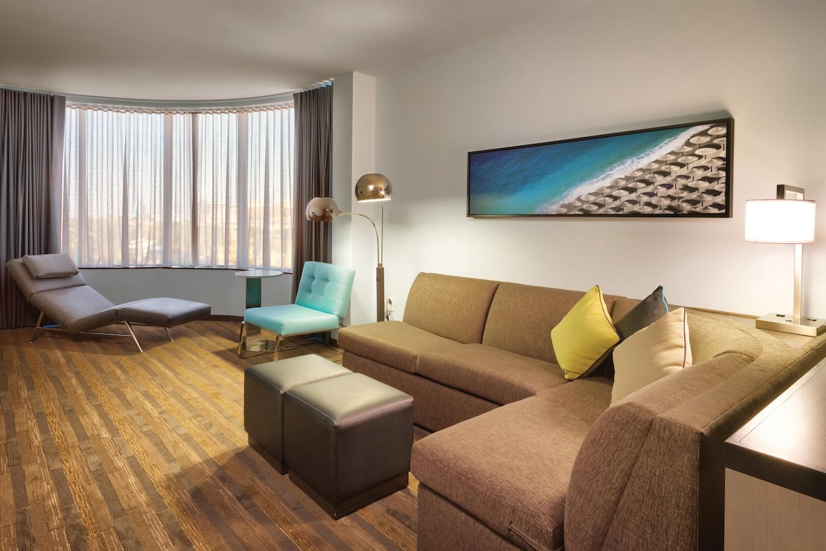 A hotel room with a sofa, armchair, ottoman, and a TV.