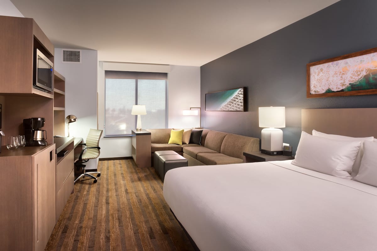 A hotel room with a large bed, a sofa, a desk with a computer, a coffee maker, and a TV.