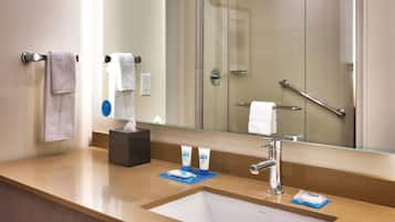 A hotel bathroom with a sink, mirror, and shower.