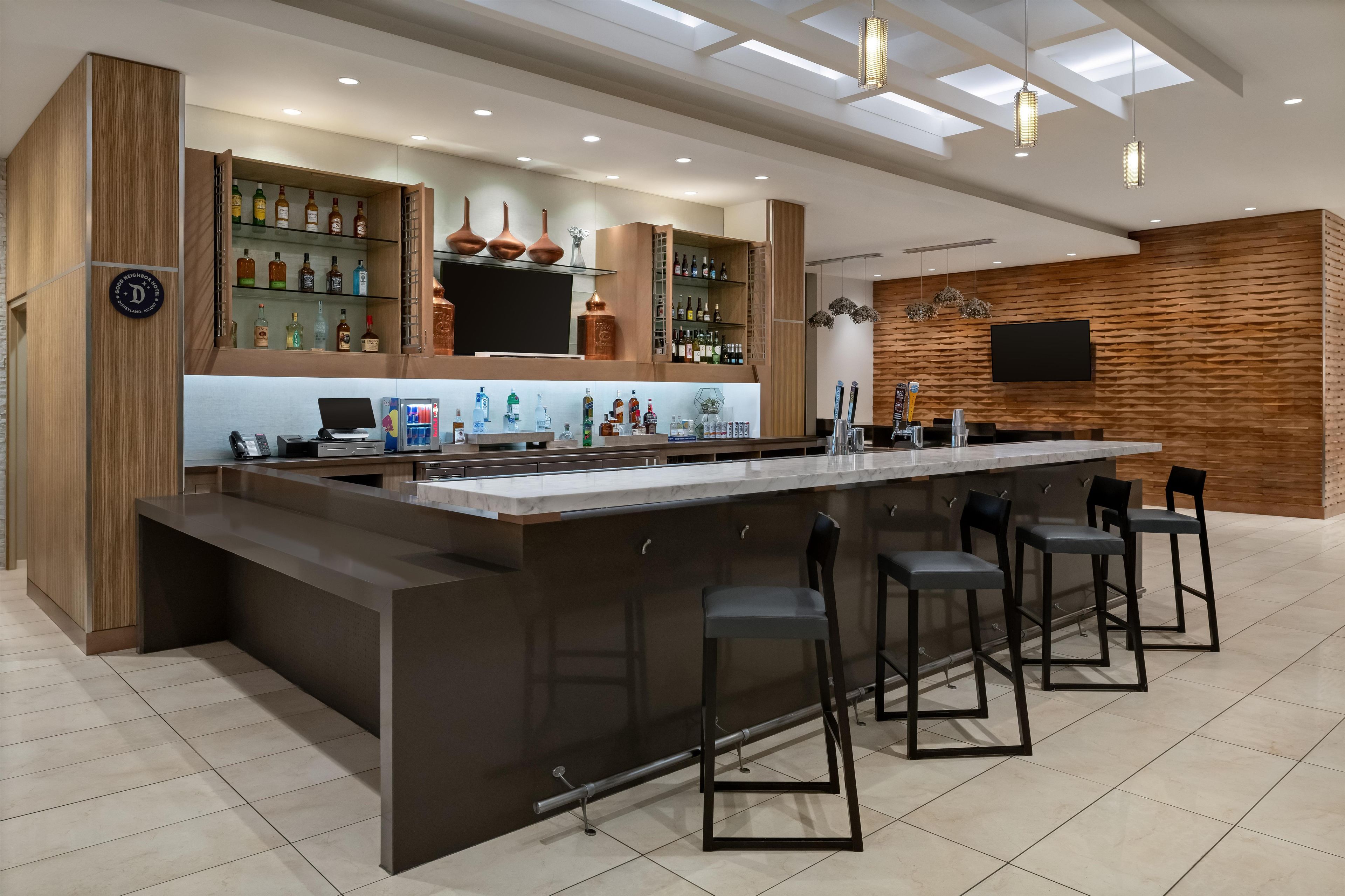 A modern bar area with a long counter, bar stools, and a variety of liquor bottles.