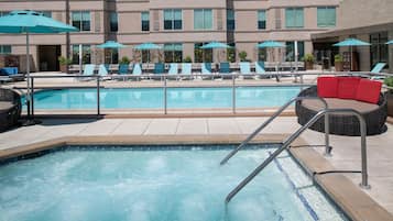 A swimming pool with lounge chairs and umbrellas, surrounded by a building with multiple floors and windows.