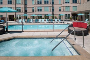 A swimming pool with lounge chairs and umbrellas, surrounded by a building with multiple floors and windows. - Hyatt House at Anaheim Resort/Convention Center (Anaheim)