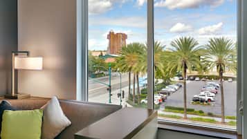 A hotel room with a large window offering a view of a parking lot, palm trees, and a distant building.