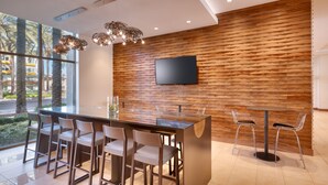 A modern bar area with a wooden wall, a flat-screen TV, and a glass-top bar counter with bar stools. - Hyatt House at Anaheim Resort/Convention Center (Anaheim)