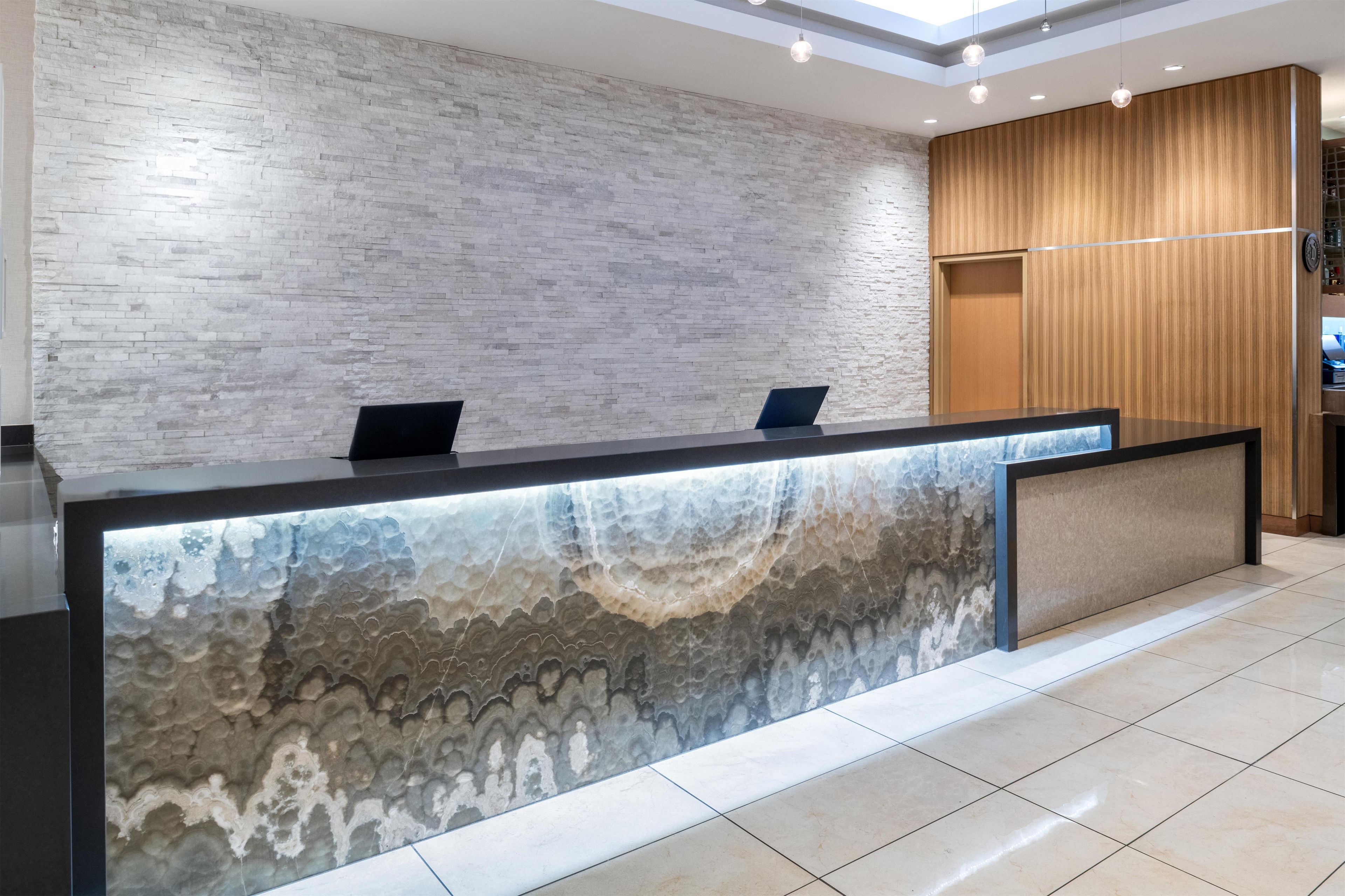 A reception desk with a marble-like design, a wooden panel wall, and a tiled floor.