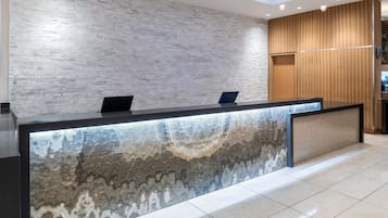 A reception desk with a marble-like design, a wooden panel wall, and a tiled floor.
