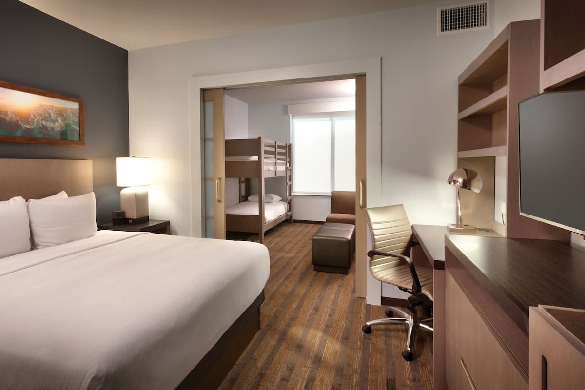 A hotel room with a large bed, a desk with a chair, a bunk bed, and a television.