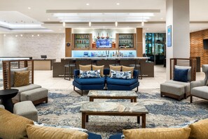 A modern lobby with a bar area, seating arrangements, and a large window.