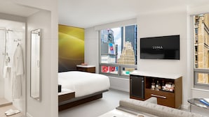A modern hotel room with a bed, a sofa, a TV, and a window with a city view. - LUMA Hotel Times Square (New York)