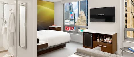 A modern hotel room with a bed, a sofa, a TV, and a window with a city view.