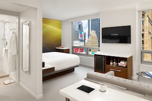 Una moderna camera d'albergo con un letto, una poltrona, una TV e una finestra vista città.