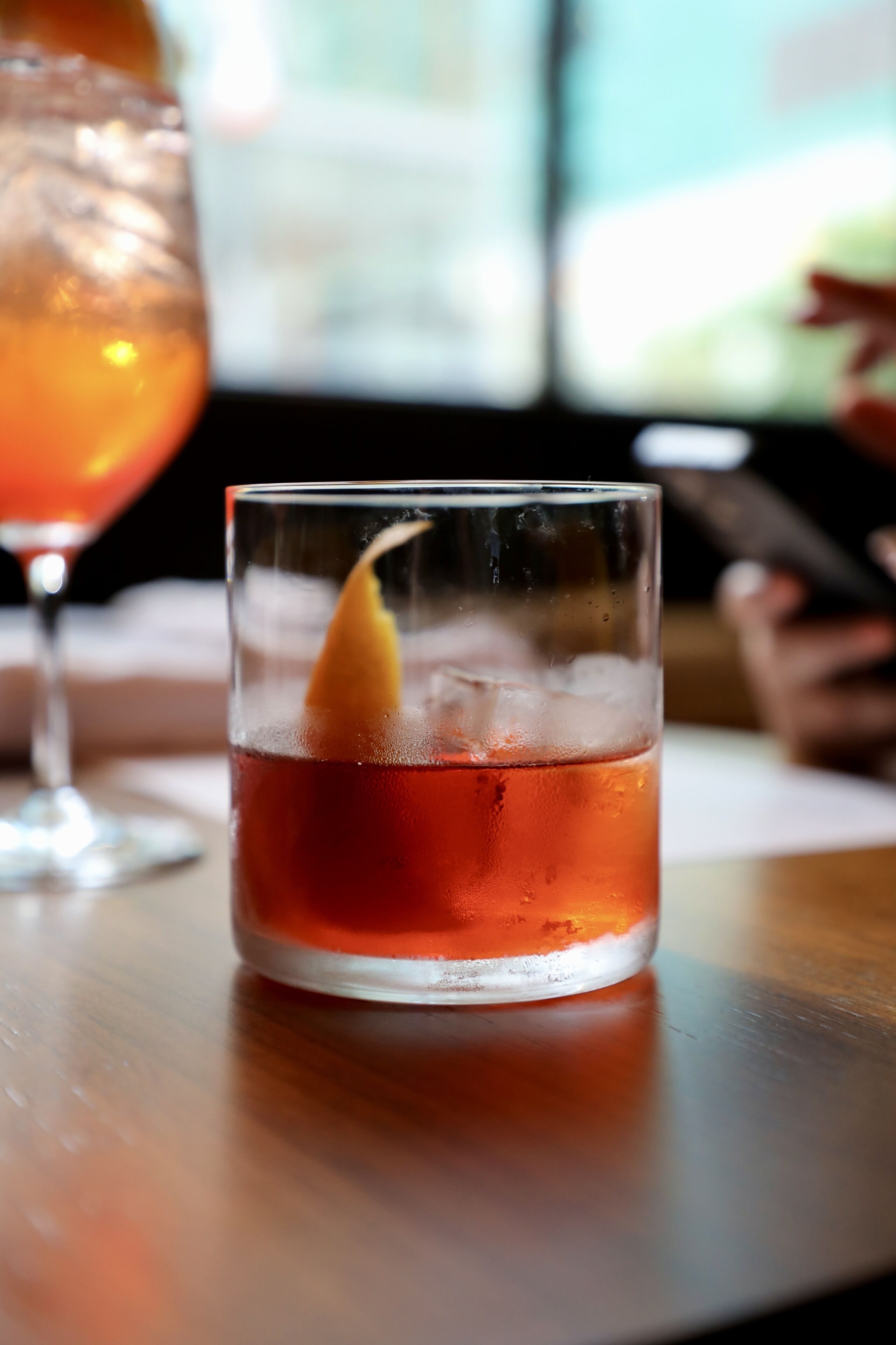 A glass of amber-colored beverage with a lemon peel garnish on a wooden surface.