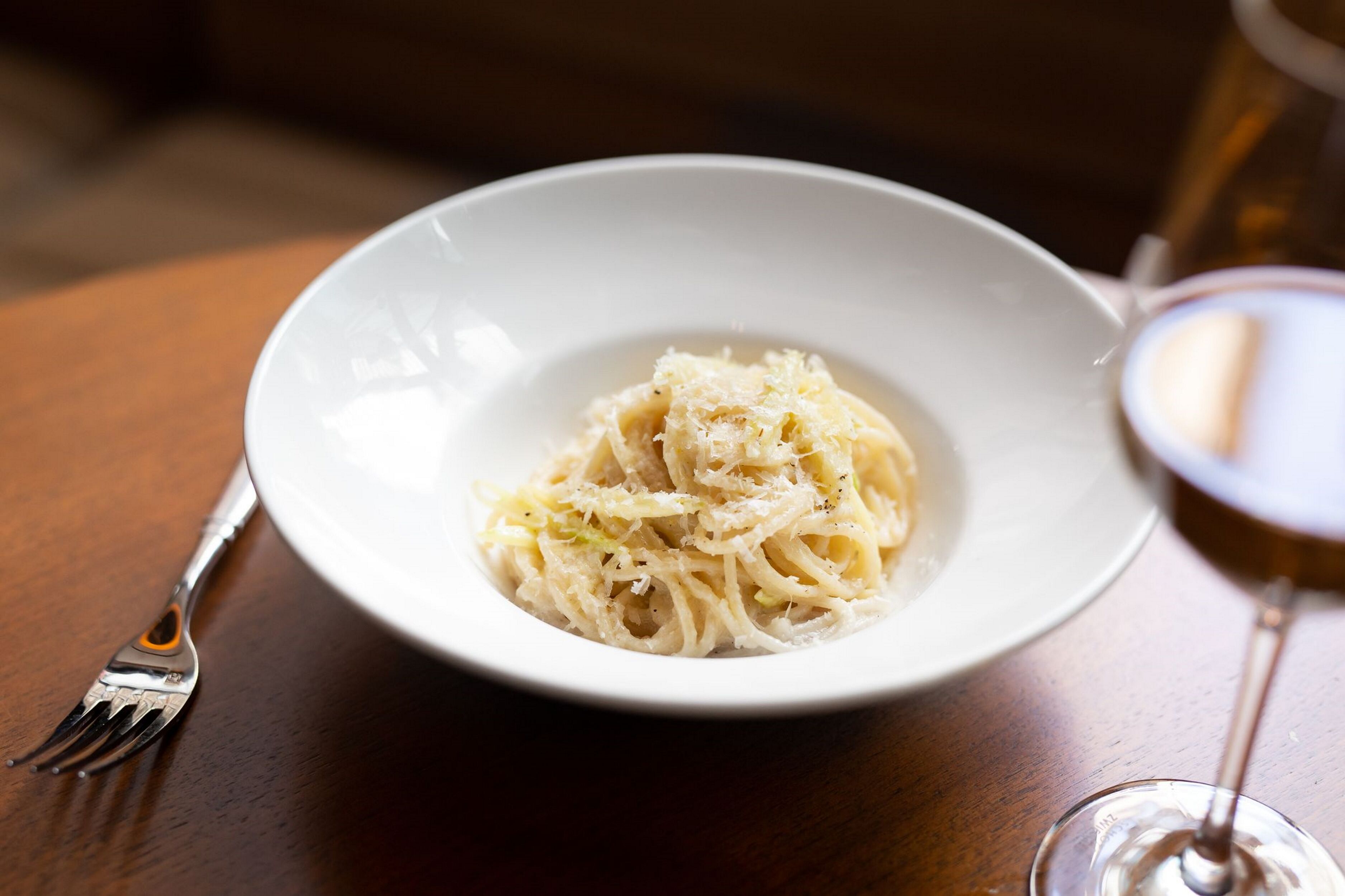 A white bowl of pasta with grated cheese on a wooden table.