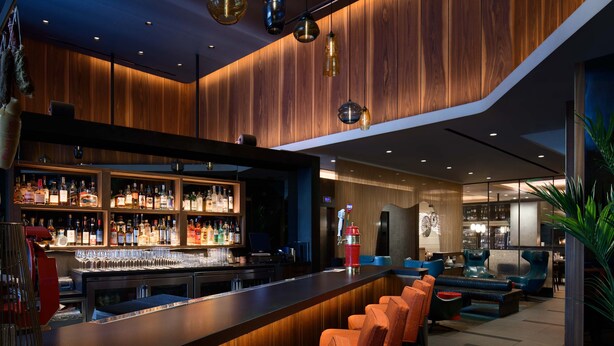 Uma área de bar com balcão de madeira, assentos e diversos frascos e copos.