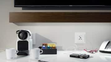 A modern hotel room with a coffee maker, two white mugs, a phone, and a pair of glasses on a white table.