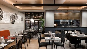 Restaurante com mesas postas para refeições, um espaço de bar e cozinha à vista.