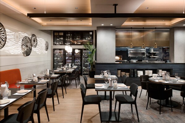 Un restaurant avec des tables dressées pour le service, un bar et une cuisine ouverte.