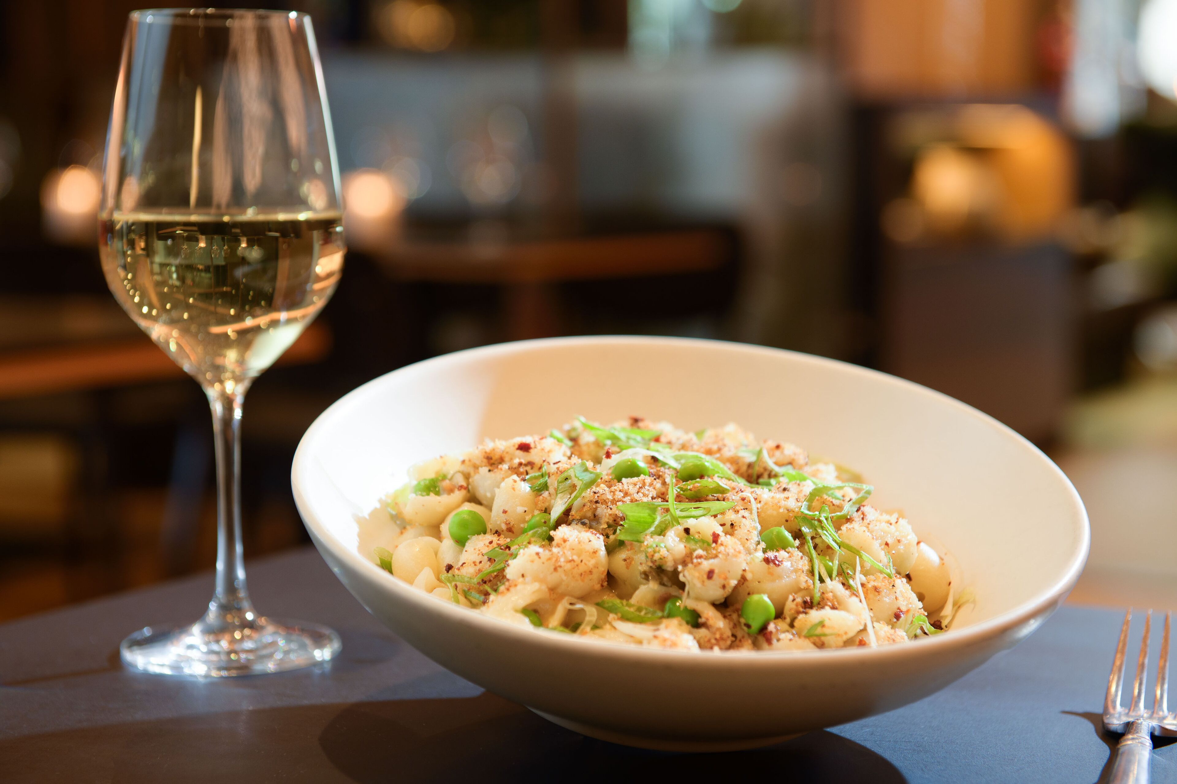 Un plato de pasta con una copa de vino blanco sobre una mesa.