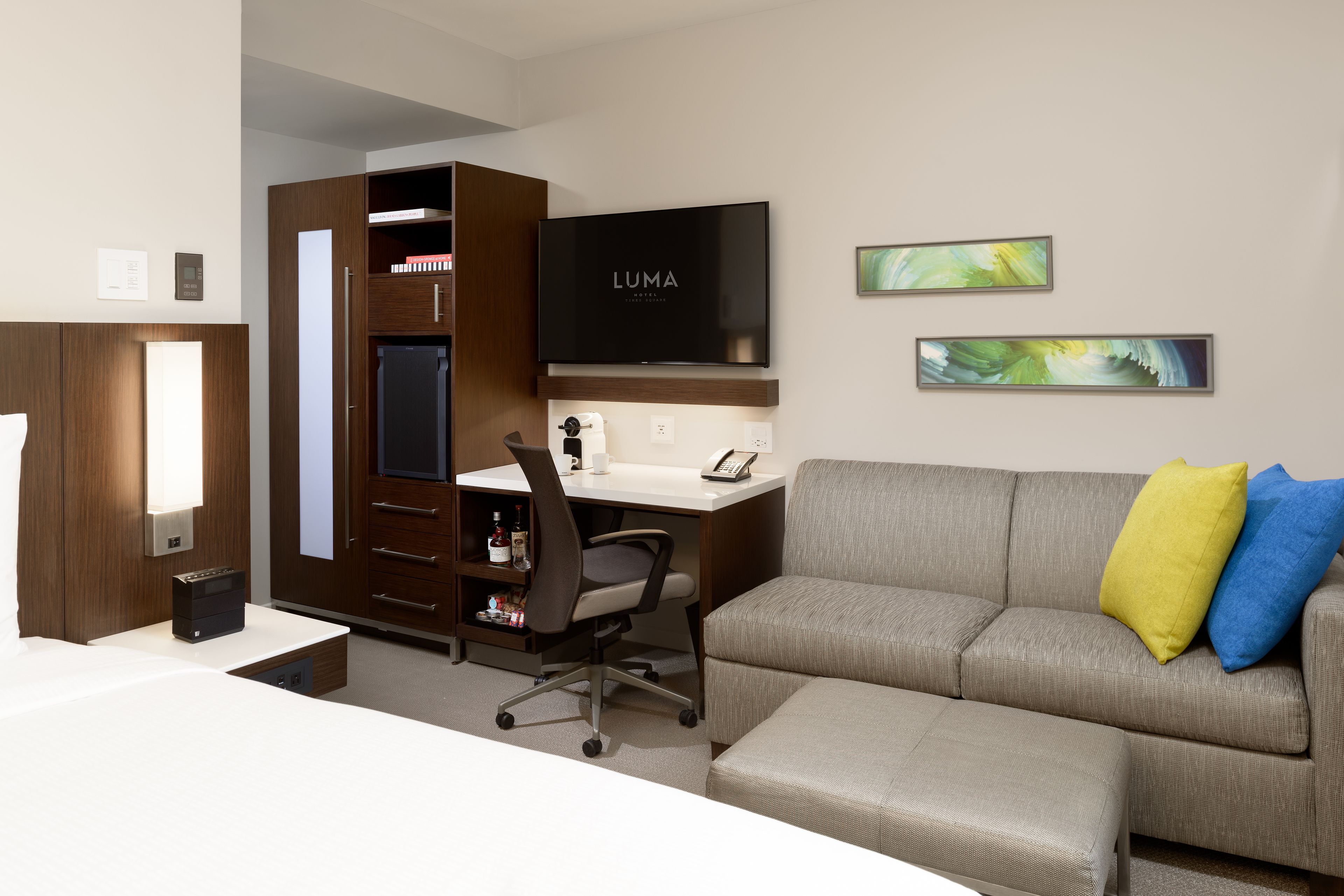 Une chambre d’hôtel moderne équipée d’un bureau, d’un canapé, d’une télévision et d’œuvres d’art accrochées au mur.