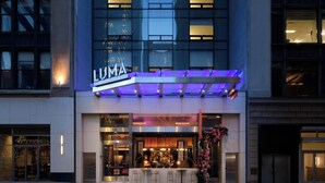 A modern building with a prominent 'LUMA' sign, large windows, and a bar area with outdoor seating. - LUMA Hotel Times Square (New York)