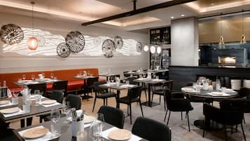 A restaurant with multiple dining tables set for guests, a bar area with a modern design, and decorative wall art.