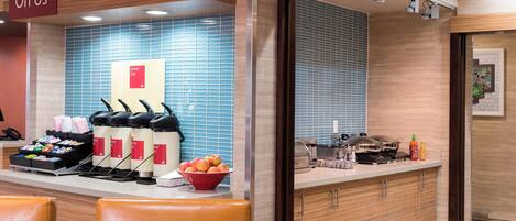 Una cocina moderna con una estación de café, un cuenco de fruta y un letrero que dice “On Us”.