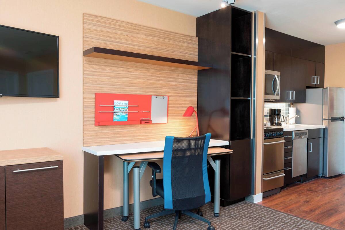 A modern kitchen with stainless steel appliances, a wooden accent wall, and a desk with a chair.