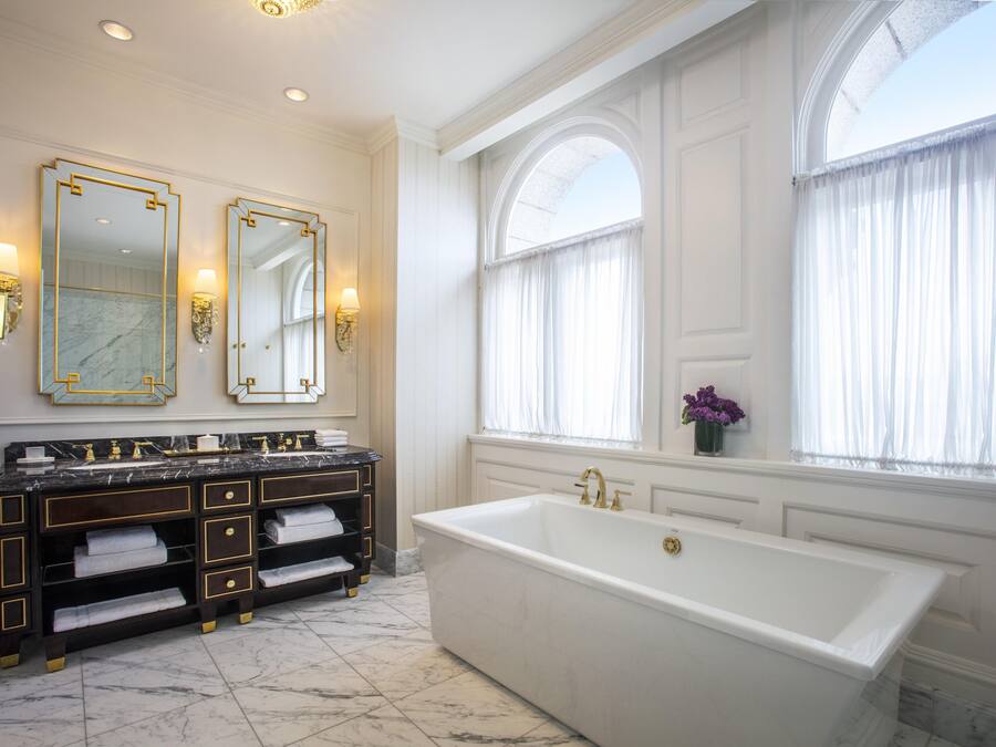 Ein luxuriöses Badezimmer mit einer großzügigen Badewanne, zwei Waschbecken mit goldfarbenen Armaturen und einem großen Spiegel.