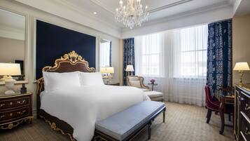 A luxurious hotel room with a large bed, a bench, a desk, and a chair.