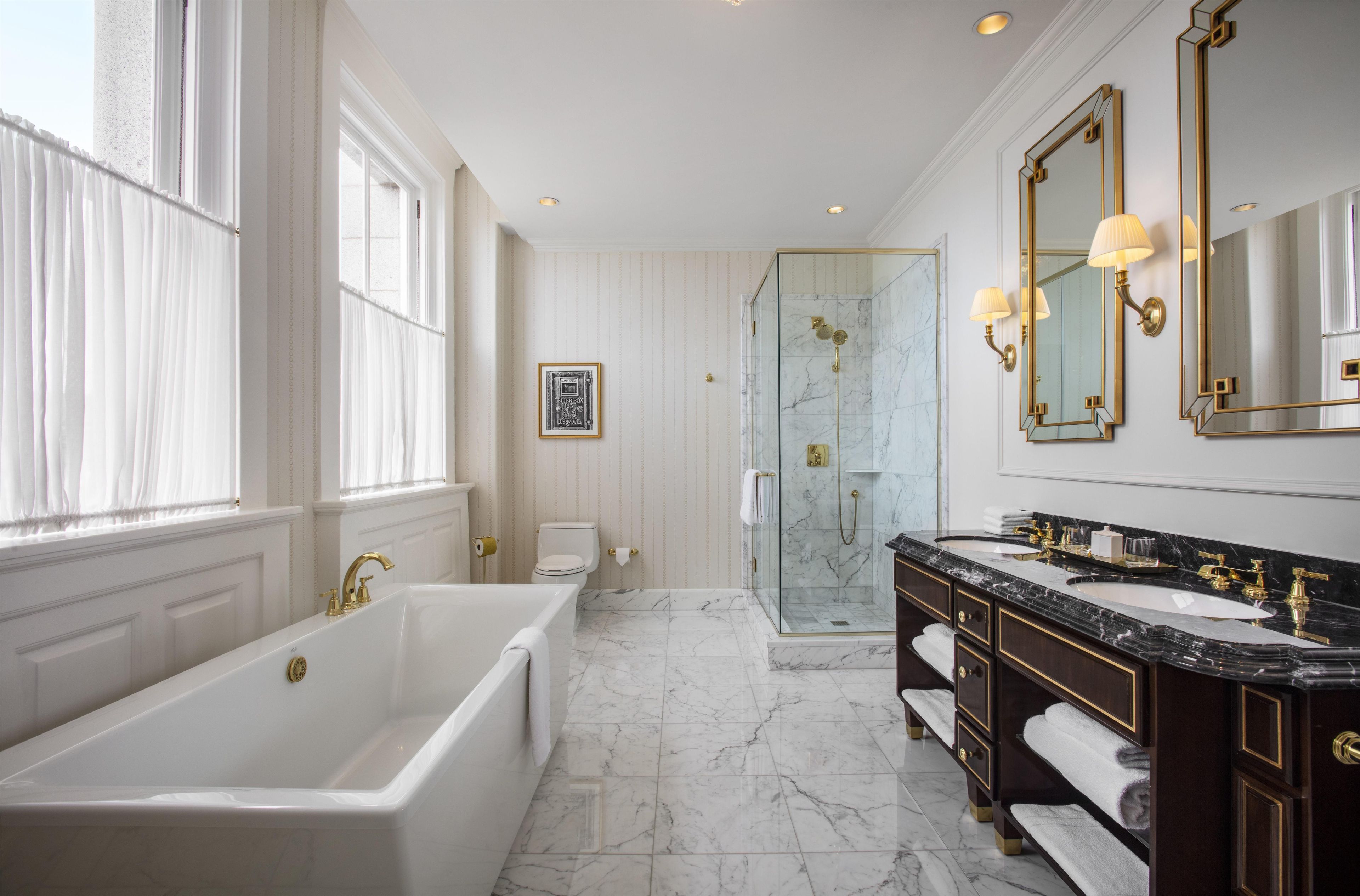Un baño lujoso con una bañera grande, una ducha envuelta en vidrio y un lavamanos doble con detalles dorados.