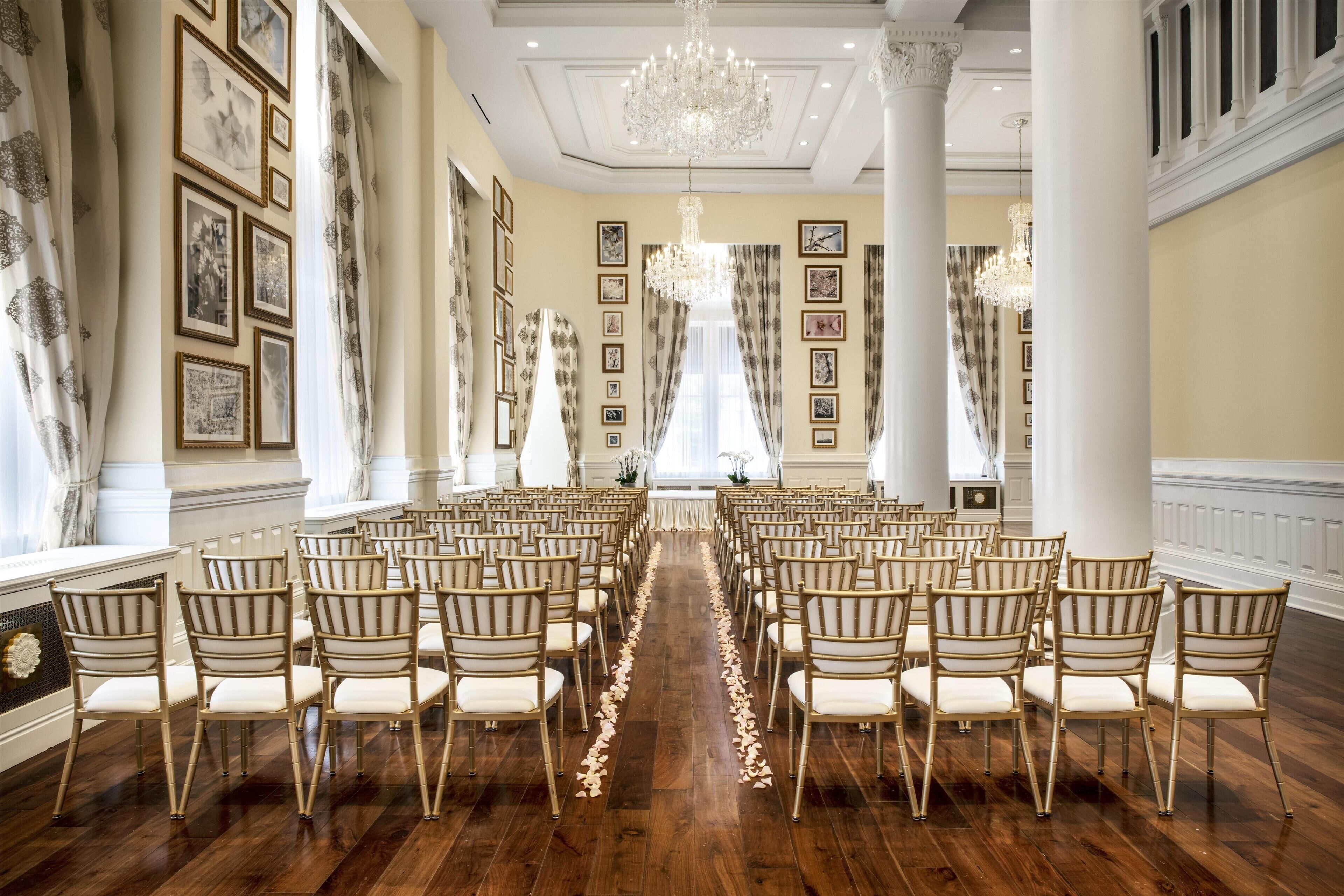 A formal room with rows of chairs, a chandelier, and framed pictures on the walls.