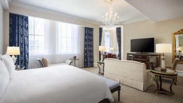 A hotel room with a large bed, a sofa, a small table, a TV, and a chandelier.