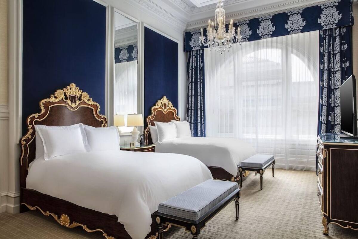 A hotel room with two beds, a chandelier, a large mirror, and a television.