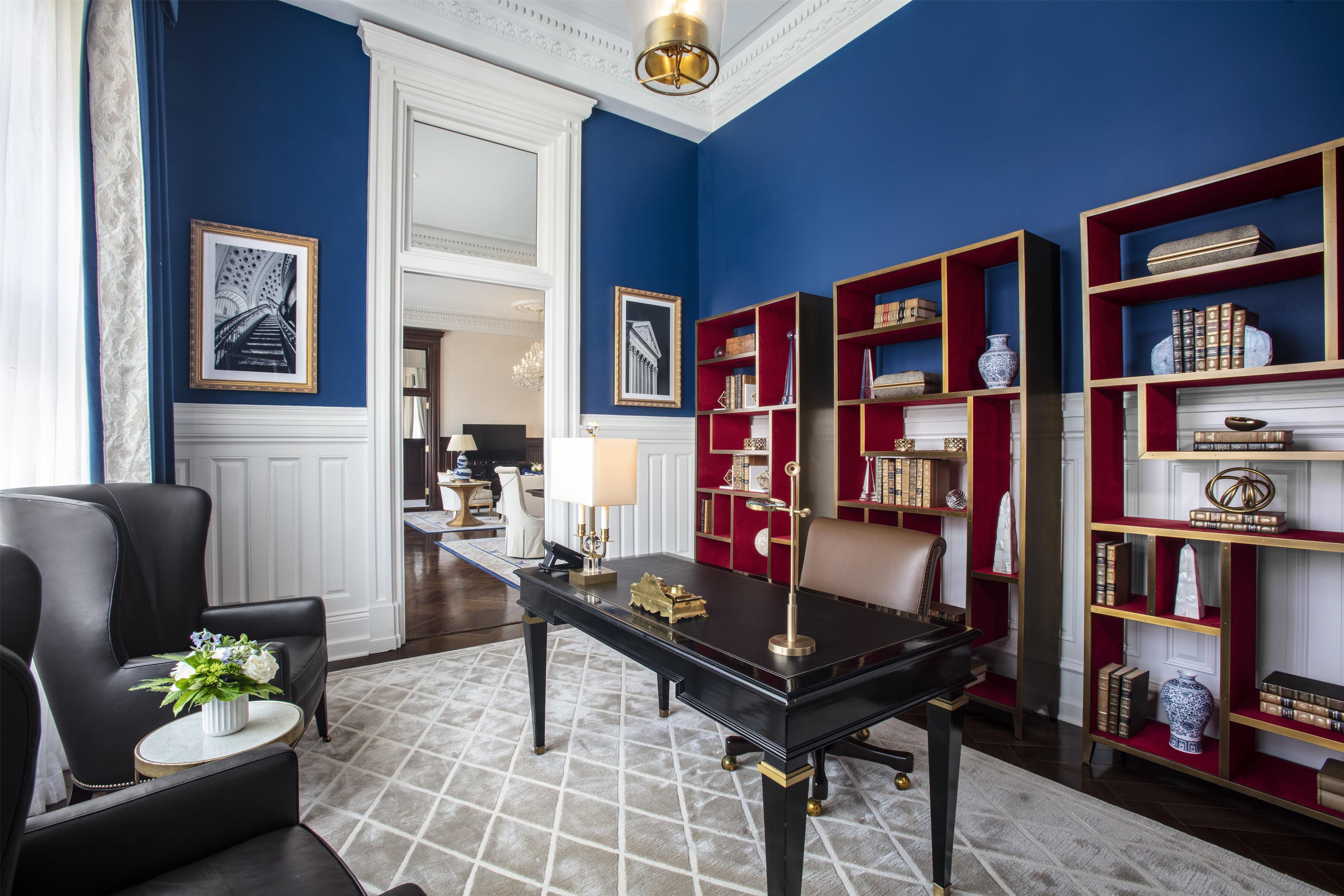 Una habitación con una mesa negra, estanterías rojas, una silla blanca y un cuadro en la pared.