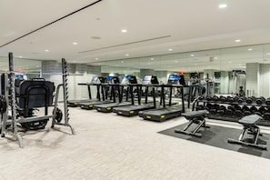 Un gimnasio con cintas de correr, máquinas de pesas y un estante con mancuernas.