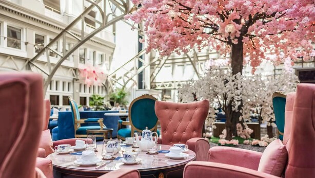 A round table set with white teacups and saucers, a teapot, and a tray, surrounded by pink upholstered chairs. - Waldorf Astoria Washington DC (Washington)