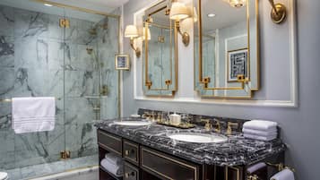 A luxurious bathroom with marble walls, a glass-enclosed shower, and gold fixtures.