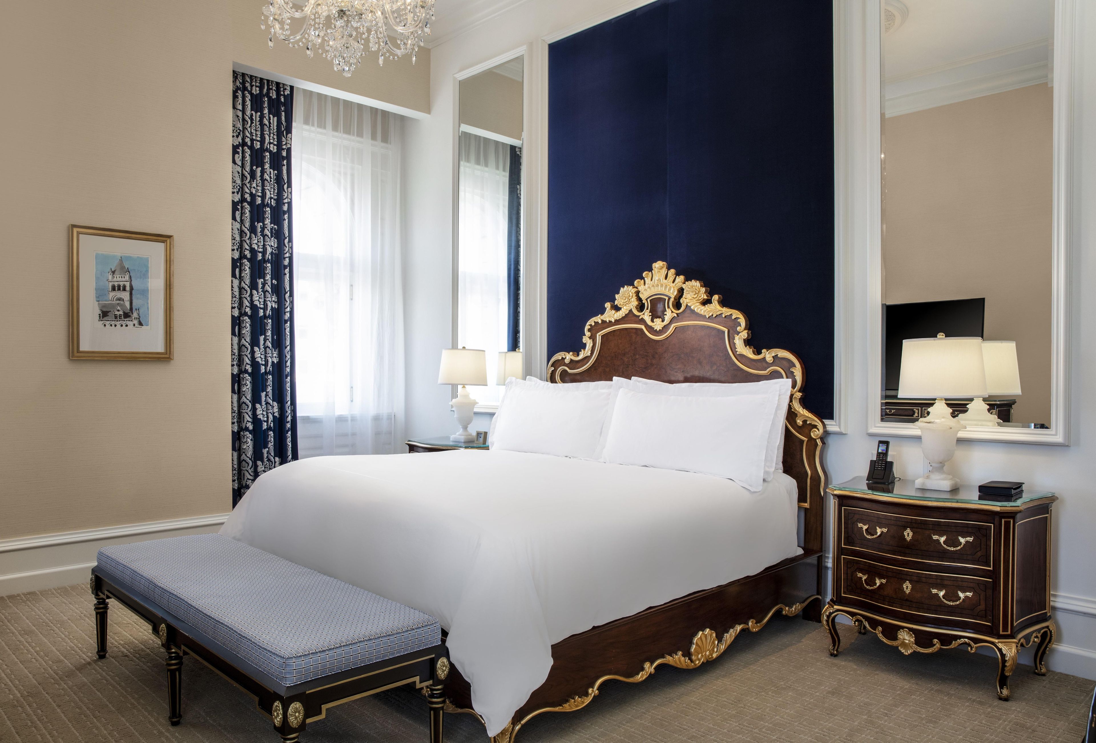 Uma cama grande com cabeceira de madeira, uma mesa de cabeceira com luminárias e um banco.