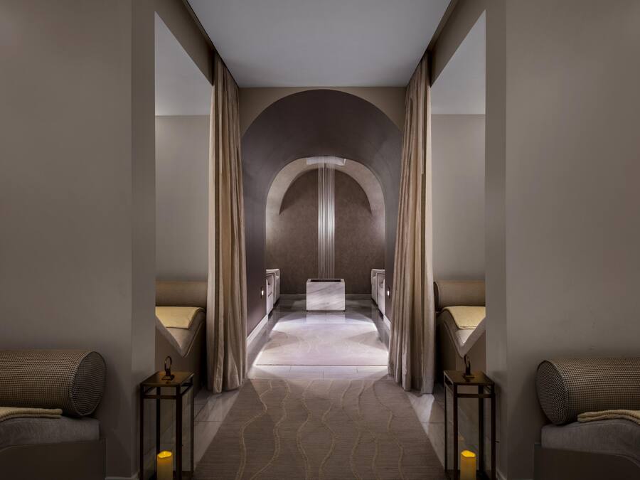A modern hotel corridor with a central arched doorway, two side beds, and a marble floor.