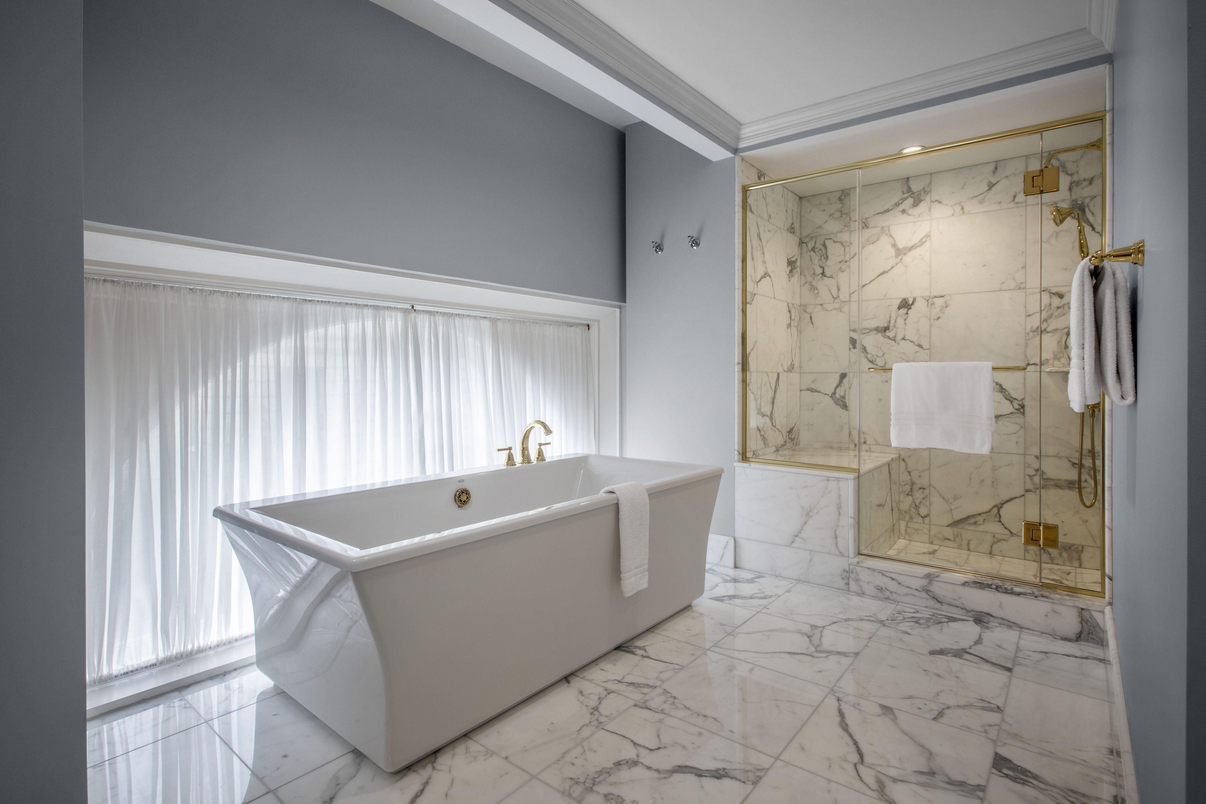 Een moderne badkamer met een vrijstaand bad, een douche met glazen wanden en een marmeren vloer.