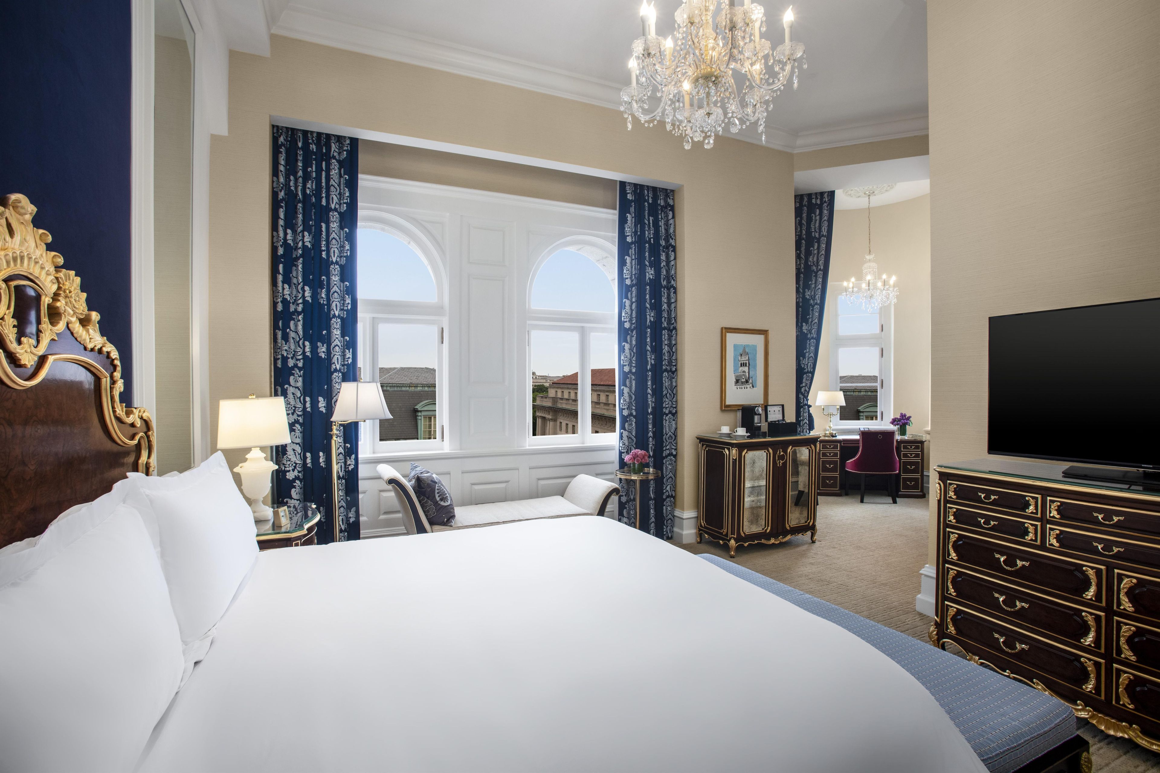 A hotel room with a large bed, a desk, a television, and a chandelier.