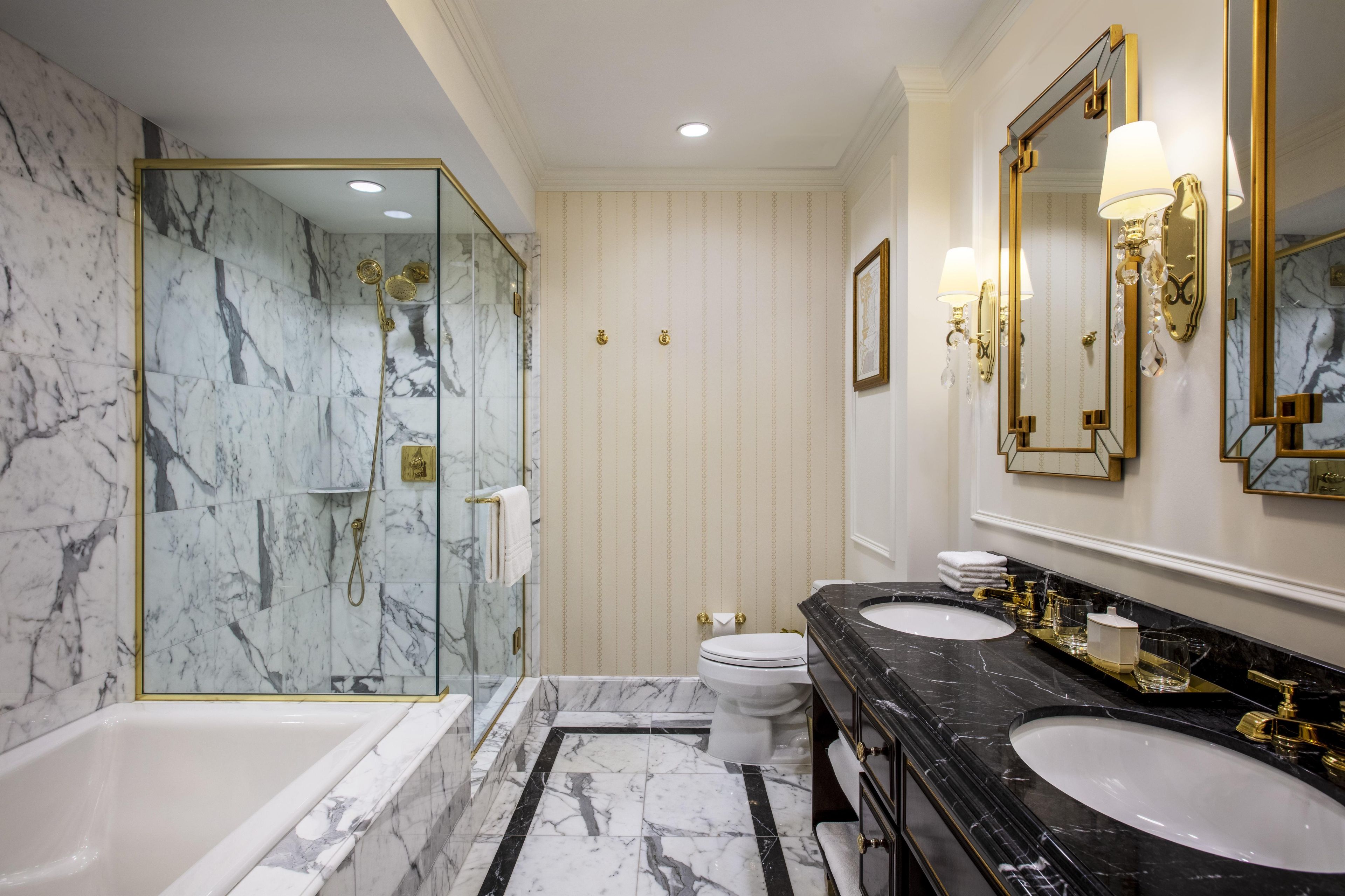 Ein Badezimmer mit Marmorwänden, einer Badewanne, zwei Waschbecken und goldenen Armaturen.
